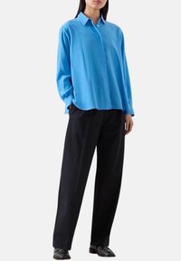 Camicia azzurra, a maniche lunghe, con bottoni e colletto, abbinata a pantaloni navy a righe sottili e scarpe nere. Tessuto dalla superficie liscia.