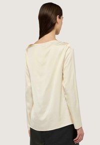 Langärmlige Bluse in Creme aus glattem Stoff mit lockerer Passform, breitem Ausschnitt und dezenten Raffungen an den Schultern.