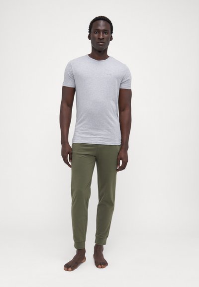 Tricou gri din bumbac, cu guler rotund, asociat cu pantaloni oliv tapered, cu mansete elastice. Modelul stă desculț, cu brațele relaxate.