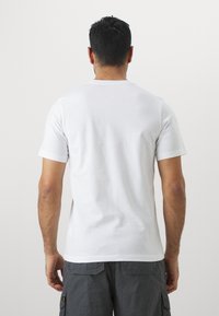 Hvid bomulds t-shirt med klassisk rund hals og korte ærmer, glat tekstur og en ensfarvet bagside. Båret med mørkegrå cargo-shorts.