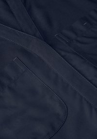 Granatowa tkanina o gładkiej teksturze, z płaskimi kieszeniami, starannym wyszyciem i minimalistycznym wzornictwem. Ogólny wygląd jest elegancki i nowoczesny.