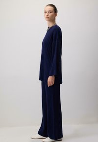 Tumed sinine sooniku muster ja laiad püksid, millel on pikad varrukad ja mugav lõige. Täiendatud tugeva hõbedase kaelakeega.