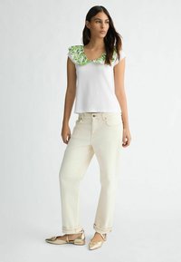 Haut blanc à manches courtes avec un col en volants floral vert, associé à un jean large crème et des chaussures plates métalliques dorées.