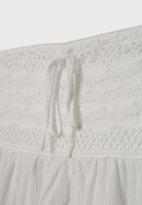 Tissu blanc avec une ceinture en crochet complexe dotée d'un cordon de serrage noué au-dessus d'un matériau de jupe léger et froncé.