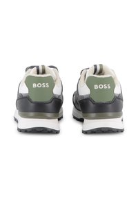 Baskets de sport noires et grises avec des accents verts, tissu texturé et semelles en caoutchouc. Logo "BOSS" affiché dans la zone du talon.