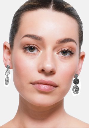Boucles d'oreilles pendantes en argent avec deux charms ovales texturés, l'un poli et l'autre mat, montés sur un clou rond.