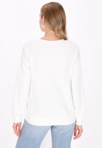 Maglione bianco a maniche lunghe con vestibilità rilassata, polsini e orlo a coste. Tessuto morbido e scollo ampio, abbinato a jeans in denim azzurro chiaro.