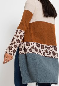 Stickad cardigan med färgblockdesign i rost, kräm och teal, med leopardmönstrade detaljer på ärmarna, texturerad tyg och avslappnad passform.