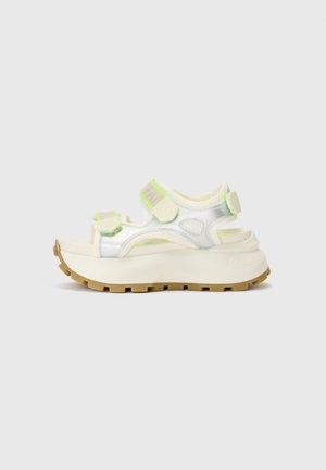 Sandalia con suela gruesa y parte superior metálica plateada. Presenta acentos en verde neón y correas ajustables para un ajuste seguro.