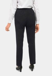 Zwarte, elastische broek met rechte pijpen, gecombineerd met een witte blouse met lange mouwen en zwarte hakken. Soepele stofstructuur.