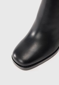 Stivale in pelle nera con punta rotonda e tacco basso su uno sfondo chiaro uniforme.