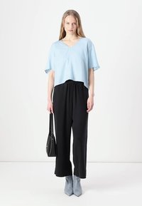 Lyseblå cropped topp med korte ermer, kombinert med svarte høyhøstede bukser og grå hælede ankelstøvler. Svart håndveske inkludert.
