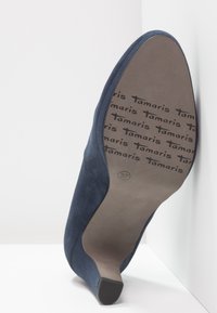 Escarpin en suede bleu marine avec un bout pointu et un talon fin. La semelle arbore un logo imprimé et la taille "37". Texture lisse dans l'ensemble.