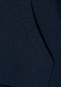 Tessuto blu marina con una texture liscia, dotato di una tasca laterale e dettagli di cucitura visibili. Design semplice e funzionale.