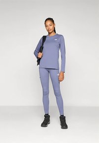 Ilgomis rankovėmis violetinė palaidinė su logotipu ir atitinkančios aptemptos tamprės, derinamos su juodais žygių batais, tinkama lauko veikloms.