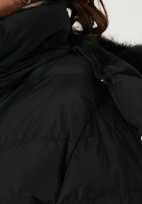 Crna podstavljena jakna s visokim ovratnikom, s glatkom vanjskom površinom i mekanim, teksturiranim podstavom. Zatvaranje na zipper i bočne džepove su vidljivi.
