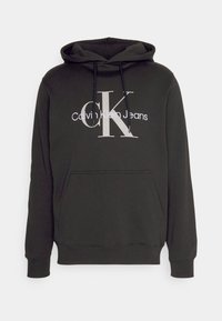 Sudadera negra con bolsillo canguro, capucha con cordón y gran logotipo en blanco de "Calvin Klein Jeans" que destaca un prominente "CK" en plata.