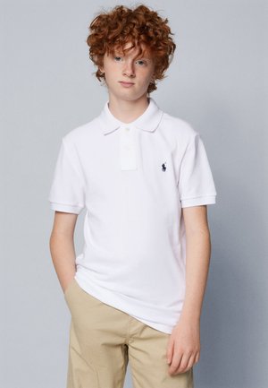 Witte polo met korte mouwen en een knoopsluiting met drie knopen, voorzien van een klein marineblauw logo op de linkerborst, gecombineerd met beige chinos.