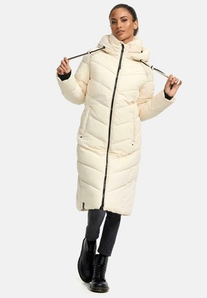 Long, cream-colored puffer coat with a hood, zigzag quilted pattern, and front zipper. Features side pockets and black trim. Black boots and dark pants.