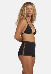 Top bikini nero con spalline sottili e pantaloni corti neri a vita alta con accenti laterali a motivo rosso e giallo. Tessuto liscio, design aderente.