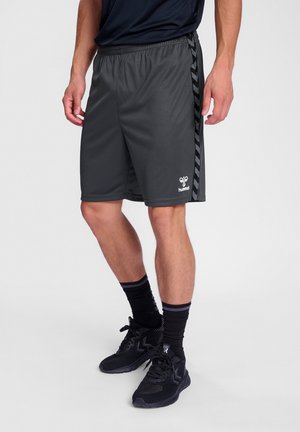Schwarze Sportshorts aus leichtem Stoff mit seitlichem Streifenmuster und kleinem Logo auf der Vorderseite. Getragen mit schwarzen Socken und Schuhen.