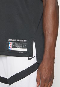 Maillot de basket-ball noir à texture en mesh, avec le texte 'MEMPHIS GRIZZLIES', étiquette Nike et logo NBA. Détail fendu sur le côté et taille 44.