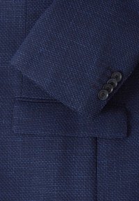 Mörkblå texturerad tygkavaj med slagkrage, som har fyra svarta knappar på ärmarnas manschetter och en ficka framtill.