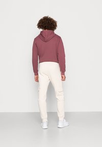 Vinröd croppad hoodie med huva, kombinerad med crèmefärgade cargobyxor med sidofickor. Vita sneakers fullbordar outfiten.