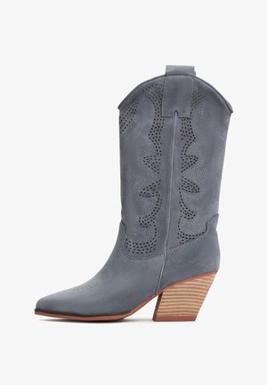 Graue Wildleder-Cowboystiefel mit einer spitzen Zehe, durchbrochener Gestaltung und einem gestapelten Holzabsatz. Mit einem dekorativen, gewellten oberen Rand.