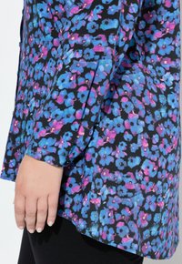 Blommig blus med svart bakgrund och blå och rosa blommor, långa ärmar och en sidoklippning för ökad rörelse. Slät tygtextur.