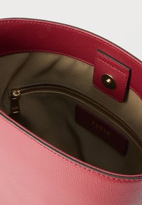 Interiorul unei genți de mână din piele roz, cu finisaj texturat, fermoar auriu, căptușeală bej și etichetă de brand vizibilă.