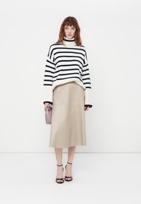 Maglione a collo alto a righe in blu navy e bianco, abbinato a una gonna midi in pelle beige. Gli accessori includono una piccola borsa viola e sandali neri.