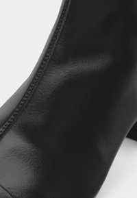 Gros plan sur une élégante botte noire en cuir, mettant en valeur la texture lisse et les coutures détaillées sur le côté.