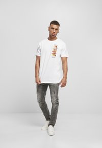 Hvid bomulds t-shirt med en vertikal grafik af stablede burgere, parret med slidte grå jeans og hvide sneakers.