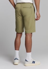 Khaki shorts met een gladde textuur, met achter zakken en een nette zoom. Gecombineerd met witte sokken en beige sneakers met marineblauwe accenten.