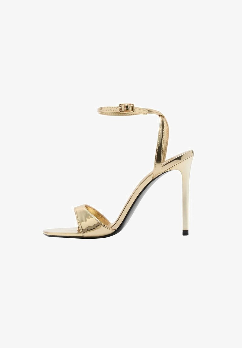 Kiilamatoit metallisé kullakarva sukkaniga, avatud varba disainiga, läikiva pinnaga ja saleda stiletto kontsaga. Musta tallaga aksent.