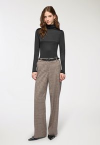 Maglione nero a maniche lunghe con colletto a imbuto abbinato a pantaloni a gamba larga in plaid a vita alta e tacchi a spillo neri; tessuto liscio e vestibilità sartoriale.