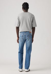 Grau Baumwoll-T-Shirt kombiniert mit hellblauen Jeans. Die Jeans verfügen über zwei Gesäßtaschen und ein braunes Leder-Brandpatch in der Nähe des Bundes.