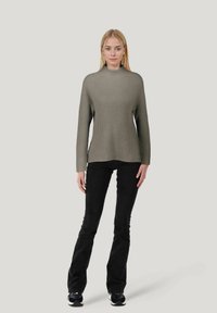Rippstrick, langärmeliger Pullover in einem gedämpften Olivton mit hohem Kragen und seitlichen Schlitzen. Kombiniert mit schwarzen Schlagjeans und Sneakers.