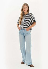 Pruhované černobílé oversized tričko, světle modré zvonové džíny a baleríny s leopardím potiskem. Obsahuje náhrdelník s přívěskem ve tvaru motýla.