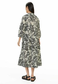 Schwarz-weißer Maxikleid mit Blättermuster, gestuftes Design, Dreiviertelärmel, leichtes Material und getragen mit schwarzen Sandalen.