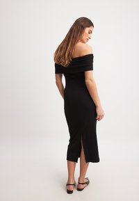 Melnas ribotas off-shoulder midi kleita ar pieguļošu siluetu, ar šķēlumu aizmugurē un gludu tekstūru, apvienota ar melnām plakanu apavu.