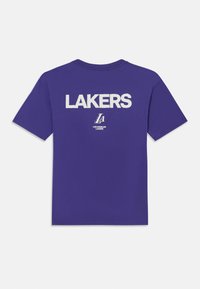 Vijolična bombažna majica s kratkimi rokavi in okroglim vratom, na zadnji strani pa je beseda "LAKERS" napisano z belimi blok črkami, pod njo pa majhen logotip.