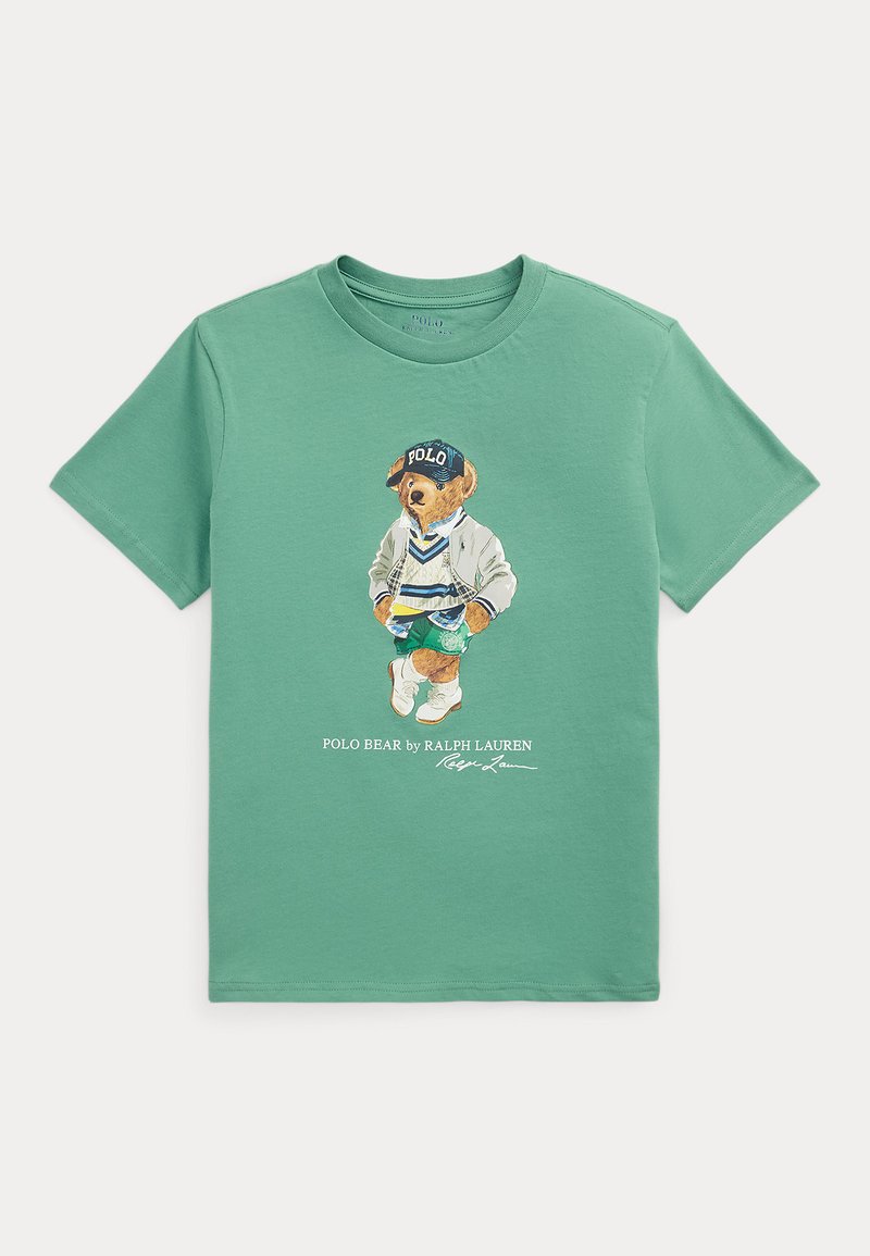 T-shirt de algodão verde menta com uma estampa de um urso vestido para o desporto, usando um boné azul, casaco em camadas e ténis brancos.