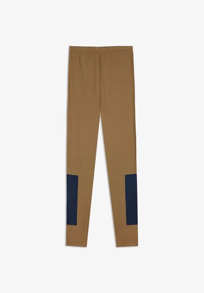 Bruine leggings met volle lengte en marineblauwe rechthoekige vlekken aan de onderste buitenkanten van elke pijp.