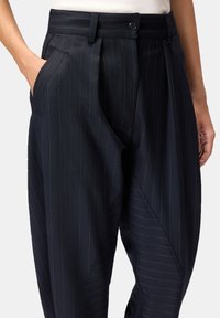 Pantalones de rayas finas azul marino con un corte ajustado, que cuentan con bolsillos laterales, cierre con botón y una textura sutil en la tela.