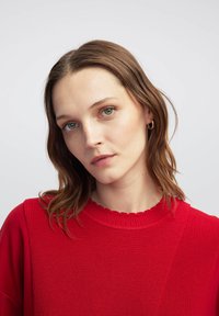 Suéter de punto rojo con un diseño de canalé texturizado y un escote con volantes, con mangas largas y un corte holgado.