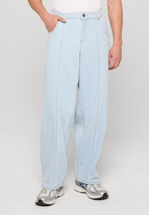 Világoskék, laza fazonú farmernadrág, amelyen hangsúlyos varrások és oldalzsebek találhatók. Szürke és kék sportcipőkkel párosítva.