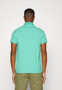 Polo en coton vert avec col, manches courtes et ourlet droit. Présente une texture lisse et des fentes latérales pour plus de confort.