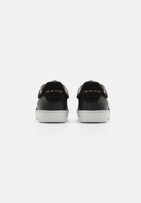 Sneaker in pelle nera con texture liscia, dotati di una suola in gomma bianca e dettagli in oro goffrato sulla parte posteriore.